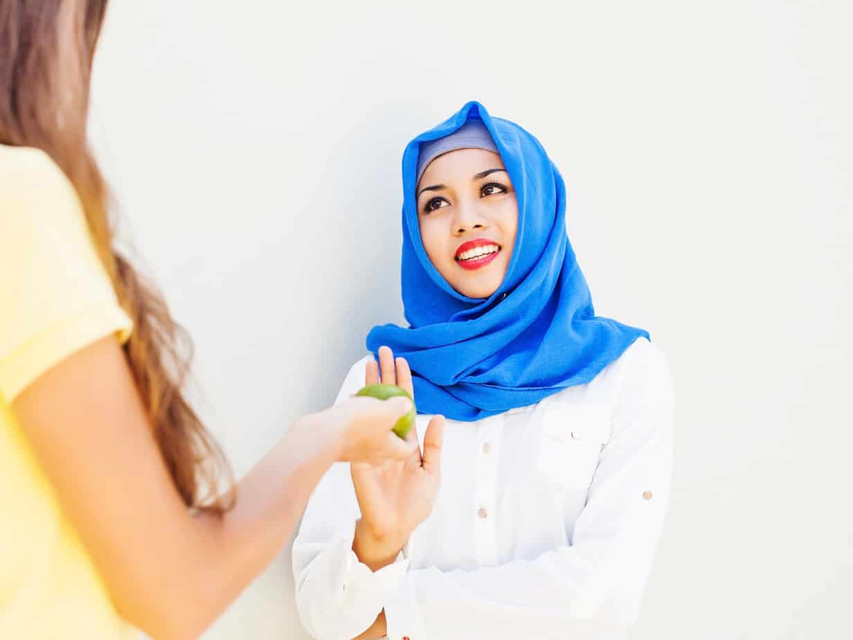 Caucasian girl stretching an apple to muslim woman